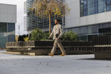 Businessman holding file folder and walking on footpath at office park - IKF01485