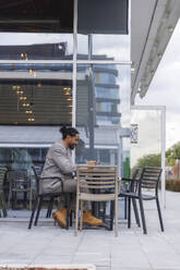 Businessman using smart phone and sitting at sidewalk cafe - IKF01505