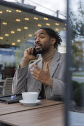 Businessman talking on smart phone at sidewalk cafe - IKF01509