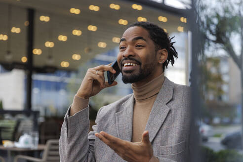 Happy businessman talking on smart phone at sidewalk cafe - IKF01511