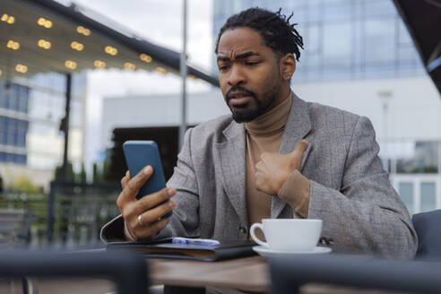 Displeased businessman talking on video call through smart phone at cafe - IKF01515