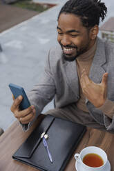 Smiling businessman talking on video call through smart phone at sidewalk cafe - IKF01519