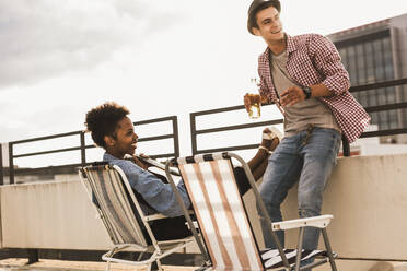 Smiling man and woman having beer on terrace - UUF30748