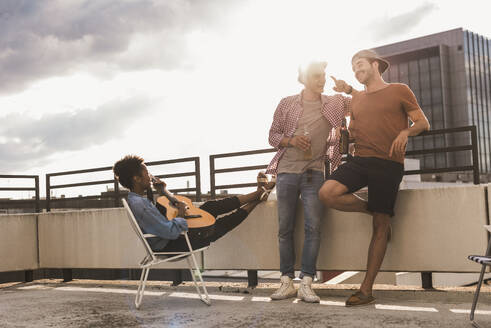 Happy friends talking and having beer on rooftop under sky - UUF30749