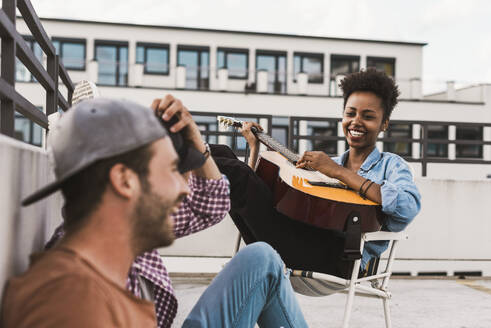 Smiling woman playing guitar near friends on terrace - UUF30753