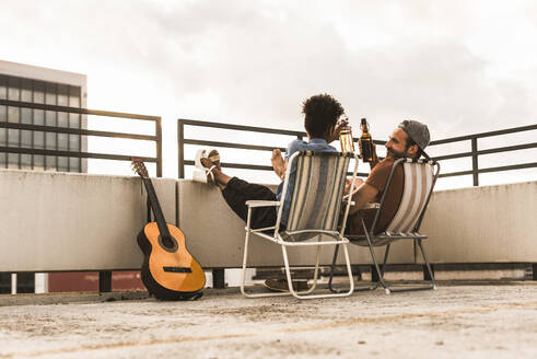 Couple toasting beer bottles and sitting on chair at terrace - UUF30755