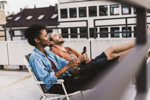 Young couple sitting with beer on rooftop - UUF30756