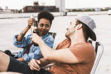 Smiling couple toasting beer bottles on terrace - UUF30757