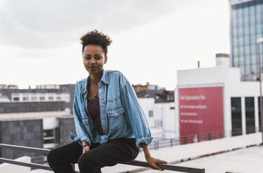 Smiling woman sitting on railing at terrace - UUF30758