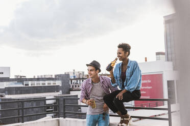 Happy couple with beer having party on rooftop under sky - UUF30759