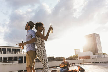 Man with woman holding beer and dancing on rooftop - UUF30768