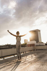 Carefree woman wearing headphones and dancing on rooftop - UUF30770