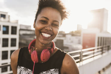 Smiling young woman with headphones on rooftop - UUF30772