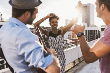 Smiling woman dancing with friends on rooftop - UUF30774