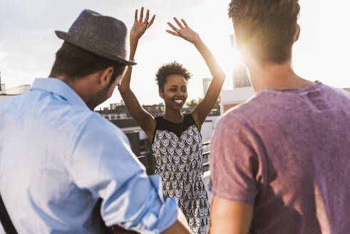 Smiling woman dancing and enjoying with friends on rooftop - UUF30775