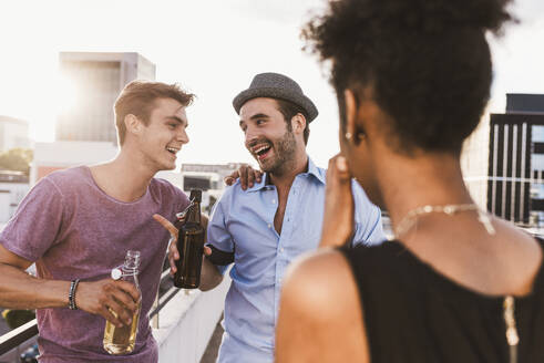 Smiling friends holding beer bottles and talking on rooftop - UUF30778