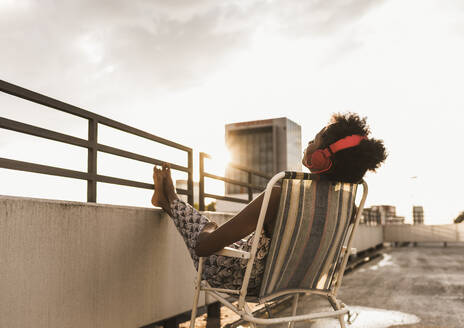 Woman wearing headphones and relaxing on rooftop - UUF30779