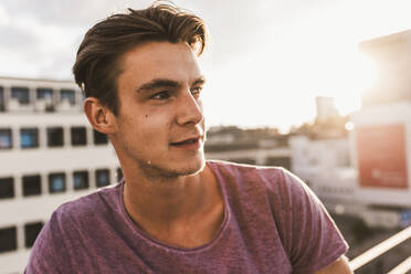 Thoughtful young man on rooftop at sunset - UUF30781