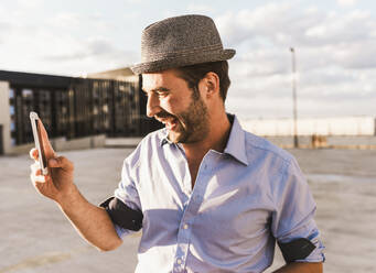 Happy man photographing through smart phone on terrace - UUF30785