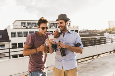 Happy man showing smart phone to friend on rooftop - UUF30787