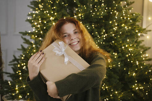 Happy woman holding gift box near Christmas tree - YBF00340