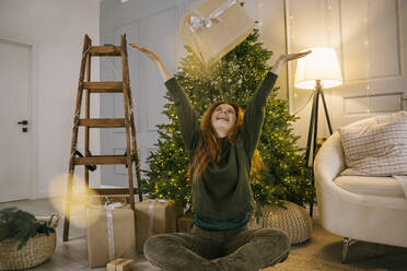 Happy woman throwing gift box near Christmas tree at home - YBF00342