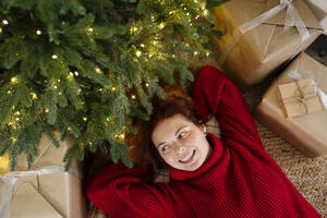 Happy woman lying near Christmas tree and gift boxes at home - YBF00351