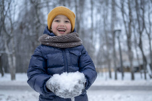 Smiling boy playing with snow in winter park - ANAF02540