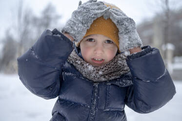 Boy touching yellow knit hat in winter - ANAF02550