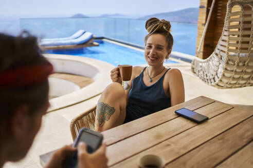 Smiling woman having tea with friend using smart phone - ANNF00794