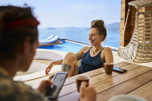 Happy woman having tea with friend using mobile phone at villa - ANNF00795