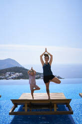 Mother and daughter doing yoga pose on deck chair near swimming pool - ANNF00799