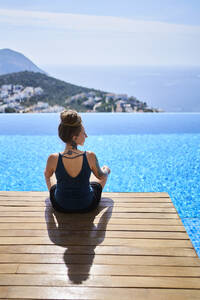 Woman relaxing on wooden platform near swimming pool - ANNF00803