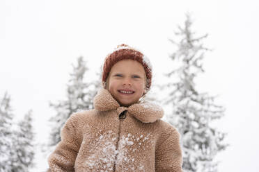 Smiling girl wearing knit hat and standing in winter forest - SVKF01784