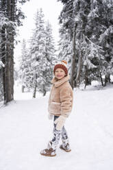 Smiling girl standing near pine trees in winter forest - SVKF01789