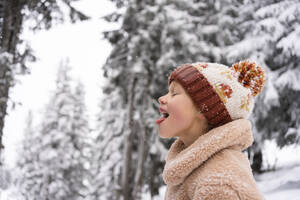 Happy girl sticking out tongue and eating snow in winter - SVKF01791