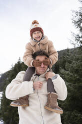 Smiling girl covering eyes and sitting on father's shoulders - SVKF01793