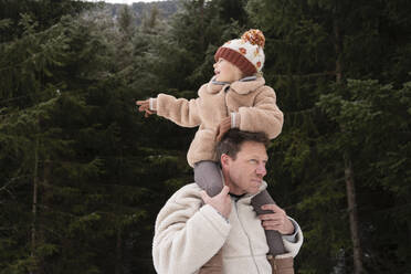 Father carrying daughter on shoulders near trees in winter forest - SVKF01794
