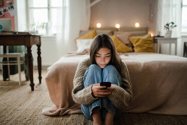 Teenager-Mädchen sitzt auf dem Boden und scrollt auf einem Smartphone. - HPIF35295