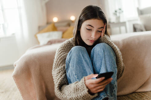 Teenager-Mädchen sitzt auf dem Boden und scrollt auf einem Smartphone. - HPIF35298