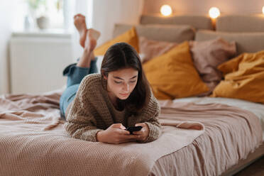 Junges Mädchen im Teenageralter rollt ihr Smartphone in einem Zimmer. - HPIF35299
