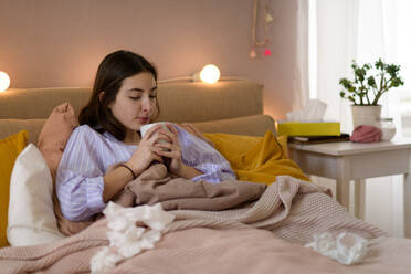 Sick teenage girl laying in bed with a cup of tea. - HPIF35331