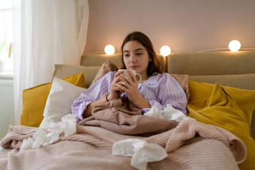 Ein krankes Mädchen im Teenageralter liegt mit einer Tasse Tee im Bett. - HPIF35333
