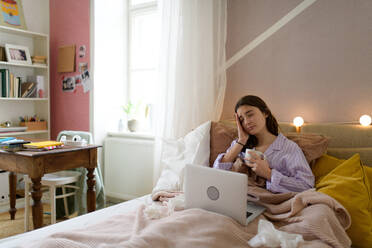 Ein krankes Mädchen im Teenageralter liegt mit einem Laptop im Bett. - HPIF35337
