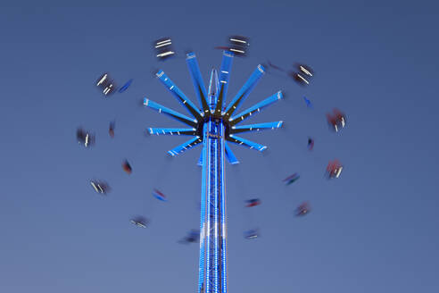 Germany, Lower Saxony, Meppen, Chain swing ride spinning against clear sky at dusk - WIF04693