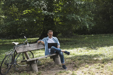 Man using laptop sitting on bench in park - UUF30796