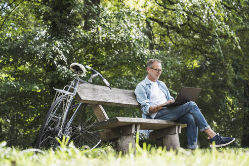 Senior man using laptop sitting on bench - UUF30797