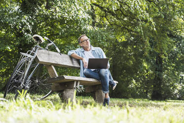 Contemplative senior man with laptop sitting on bench - UUF30800