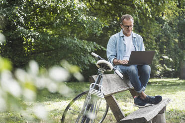 Senior man using laptop sitting on bench in park - UUF30801