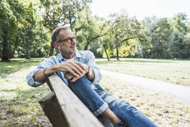 Contemplative senior man sitting on bench in park - UUF30804